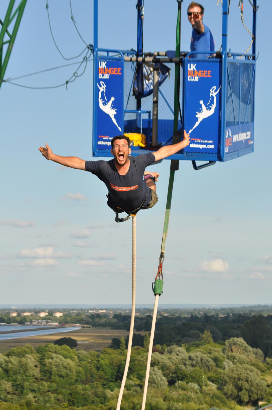 Bungee jumper leaping from the UK Bungee Club crane cage with arms outstretched at a 160ft bungee jump event