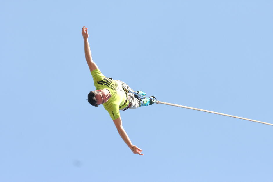 Bungee jumper upside down in freefall against a clear blue sky at a UK Bungee Club crane bungee jump